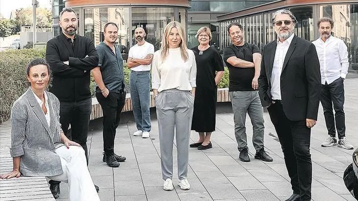 Bir grup insan, iç mekanda bir masanın çevresinde duruyor.